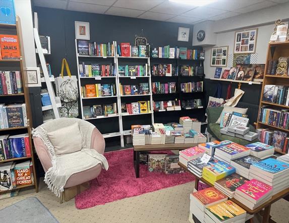 Pink seat with white rug and cushion surrounded by shelves and tables with books