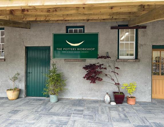 Entrance to Shearer Cermaics in grounds ofo Glenarm Castle with green door, grey paving, grey walls and green sign stating 'The Potters Workshop'