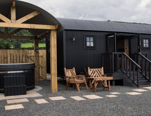 Hot tub beside a black Shepherds Hut with step entrance and seats outside at Shepherds Rest Luxury Glamping in Carnlough