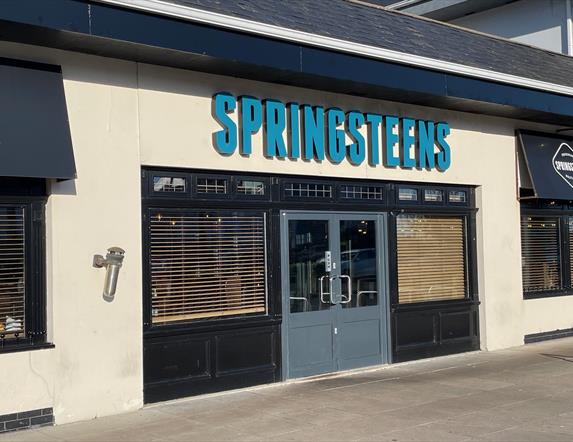 Exterior of Springsteens restaurant with grey doors and large sign.