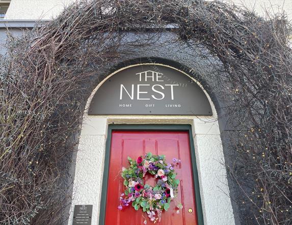 Archway over red door with sign reading The Nest and garland on the door