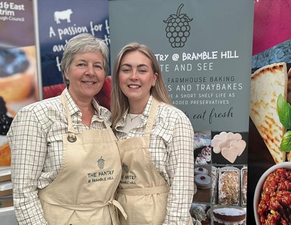 Gail from The Pantry at Bramble Hill at Balmoral Show standing in front of a display stand with a branded apron and another demonstrator