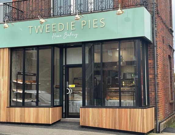 Exterior of Tweedie Pies Home Bakery with black framed glass, mint green sign and wooden panel trim