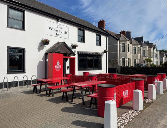 Exterior of Whitecliff Inn with red tables and chairs for seating area.