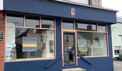 Exterior of the Gallery in Whitehead, painted blue with large windows and art displayed in them