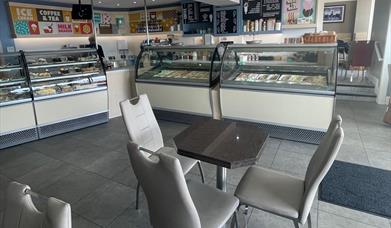 Grey seats and table with ice cream counters and food display fridges in the background