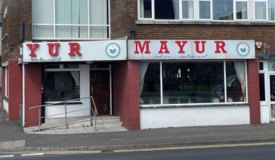 Exterior of Mayur Indian restaurant with sign in red and white, plus whote and red walls