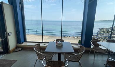 Table and seats within Prom Cafe looking out window to sea.