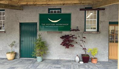 Entrance to Shearer Cermaics in grounds ofo Glenarm Castle with green door, grey paving, grey walls and green sign stating 'The Potters Workshop'