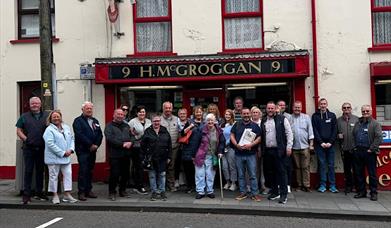 A group of people standing outside an old pub, on a walikng tour of Ballymena