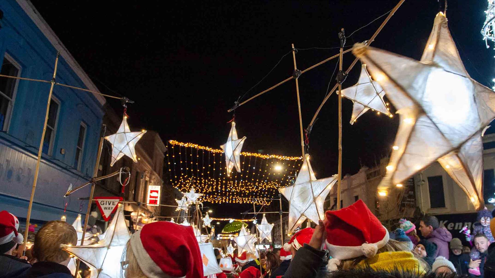People parading with star lanterns and wearing Santa hats in Ballymena town centre with Christmas lights switched on.