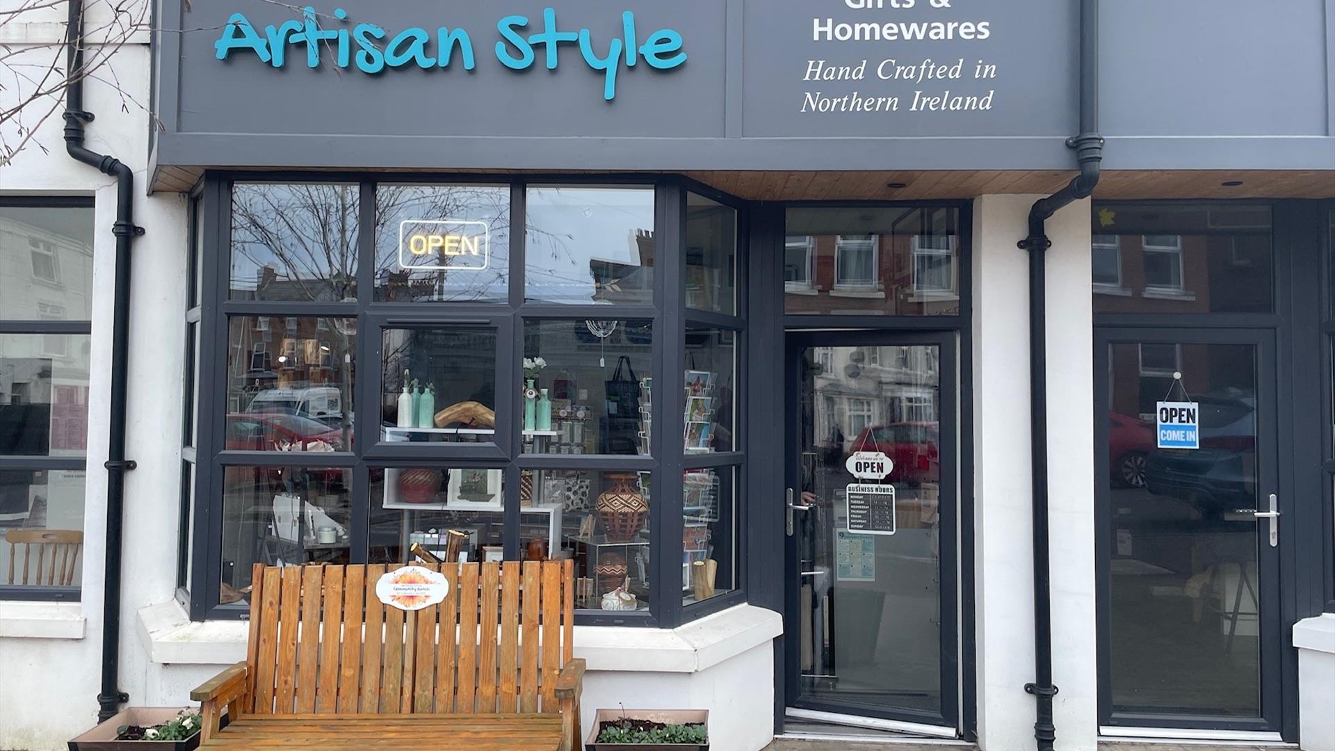 Exterior of Artisan Style shop with a seating bench and black windows and droo.