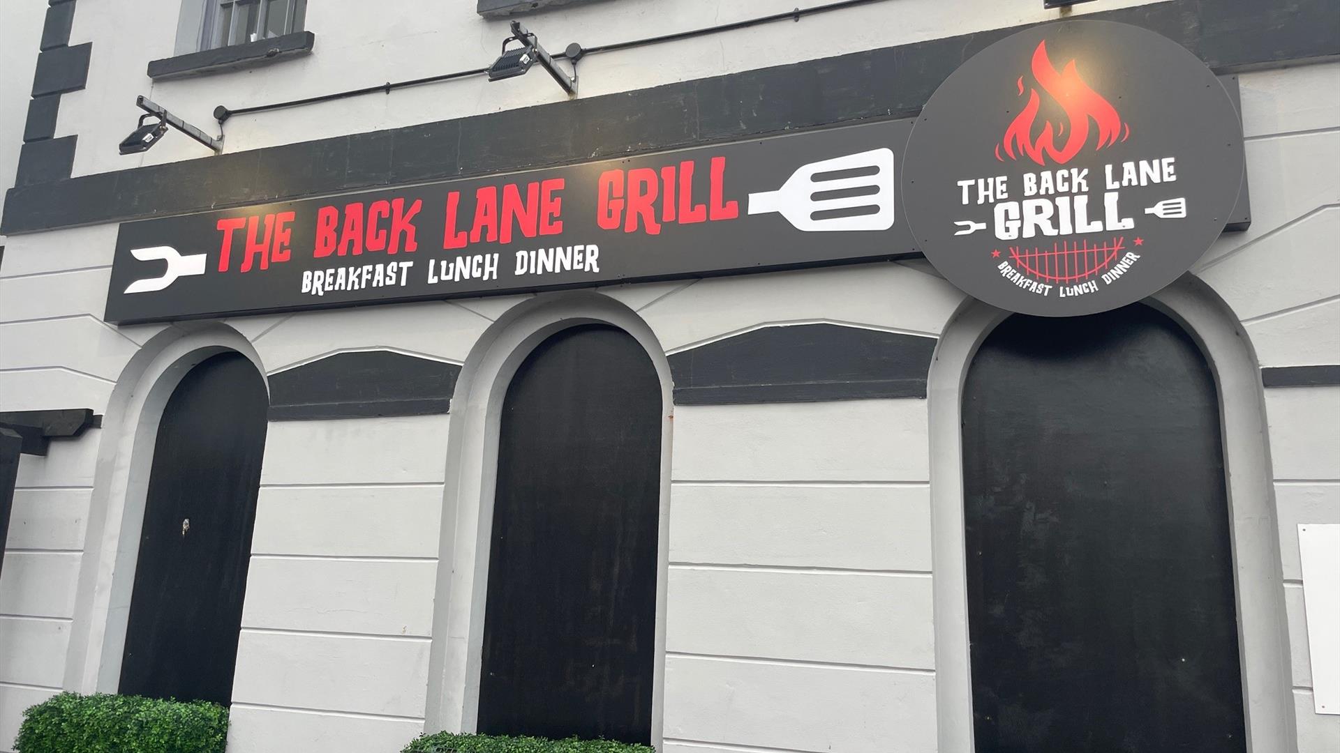 Exterior sign for The Back Lane Grill in red and white writing on black background