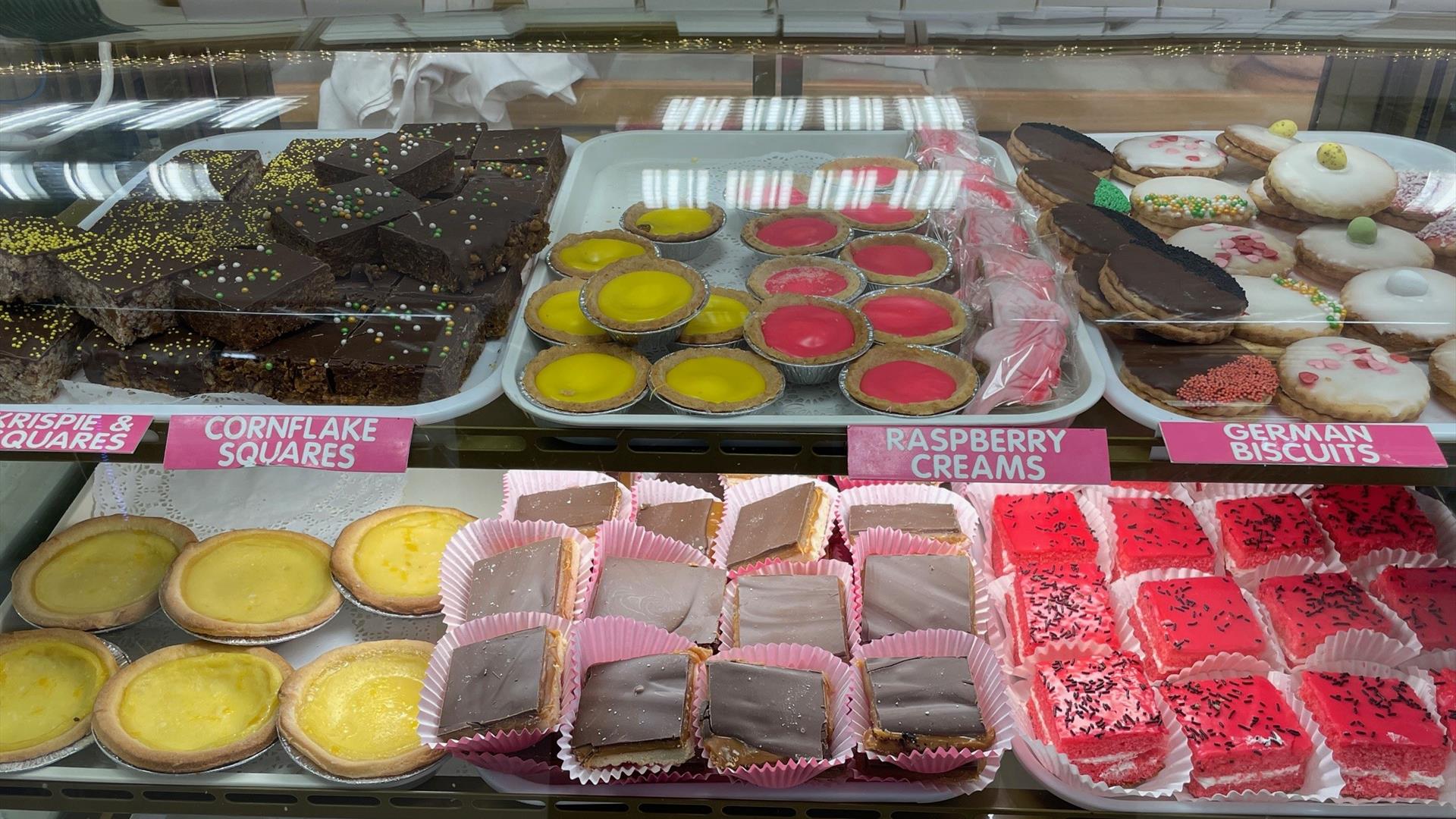 Shelf of baked treats including raspberry creams, cornflake squares and german biscuits