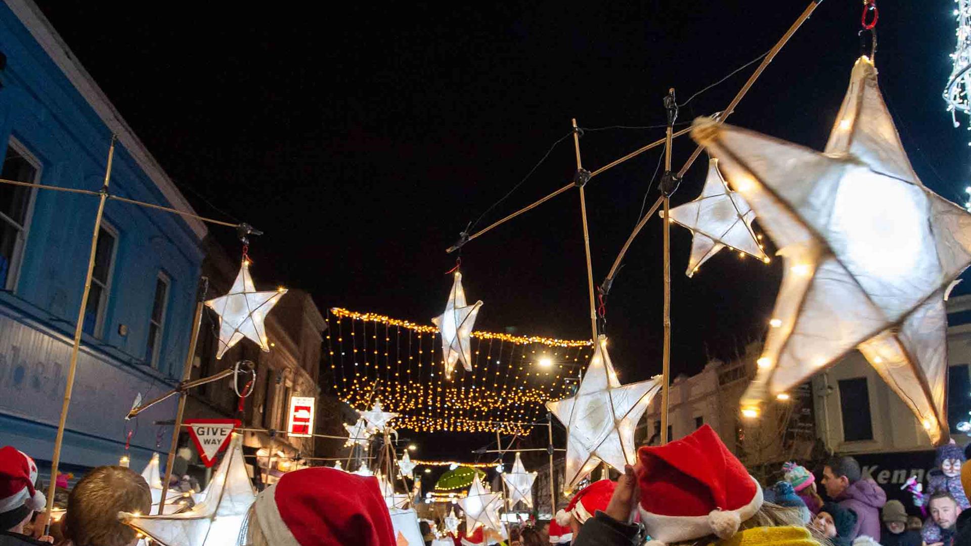 People parading with star lanterns and wearing Santa hats in Ballymena town centre with Christmas lights switched on.