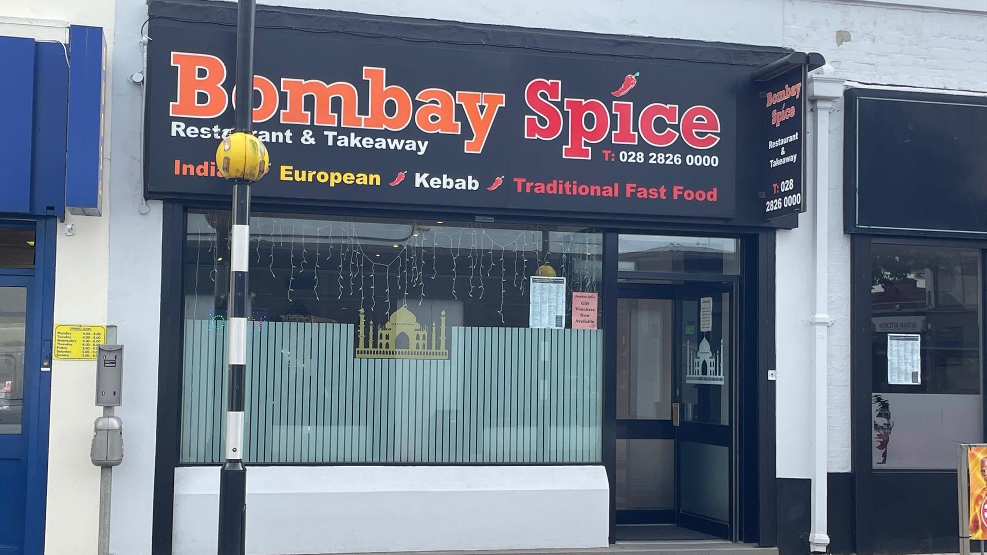 Exterior of Bombay Spice restaurant with pedestrian crossing in front of it and large window with entrance door.