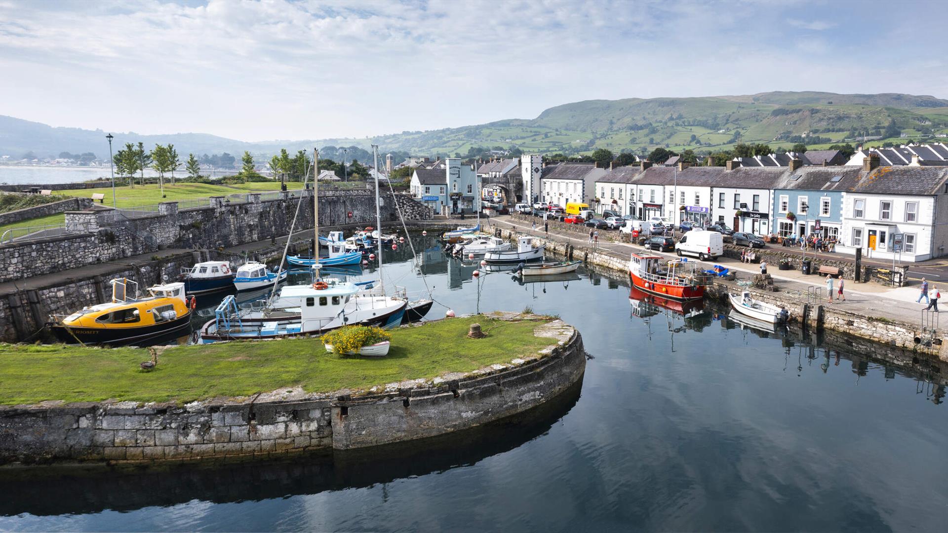 Aerial view of Carnlough Harbour with shops and homes in the background and boats in the harbour
