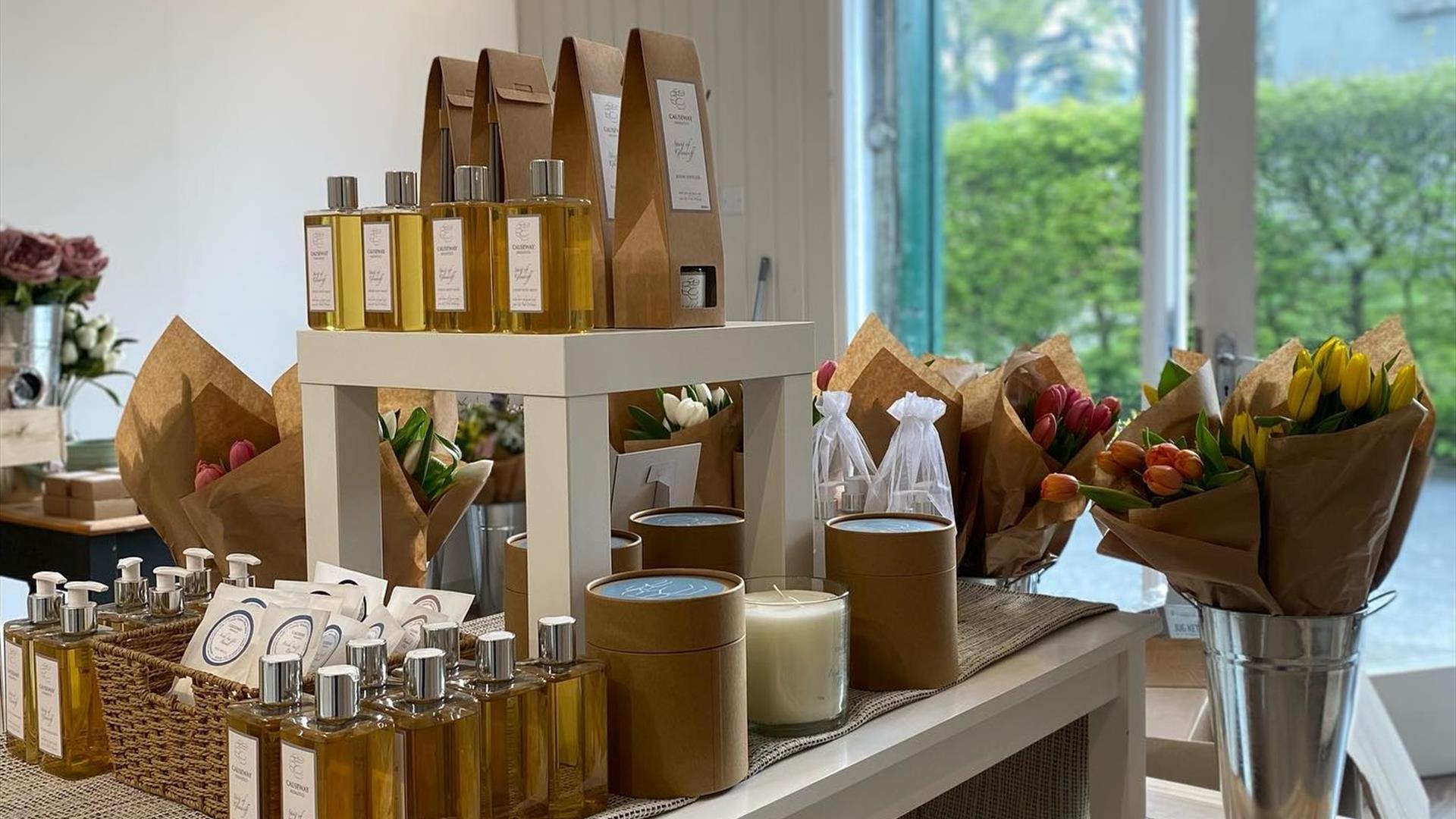 Table display of fragrances and oils with bunches of flowers in bucket displays behind.