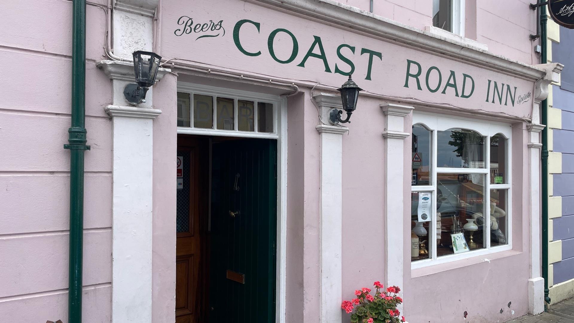 Pink exterior of Coast Road Inn in Glenarm with flowers outside and collectible window display