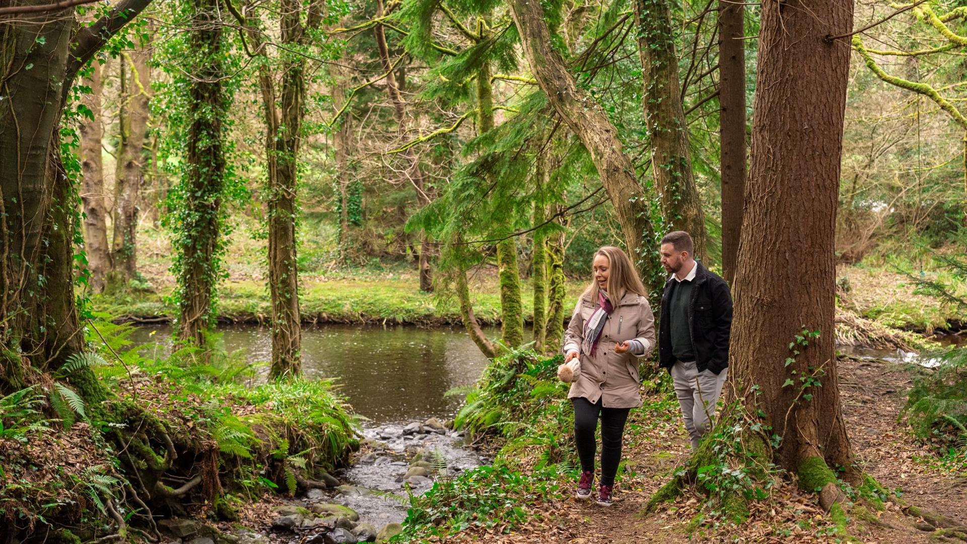 Man and woman walking alongside River in Glenarm Forest surrounded by trees