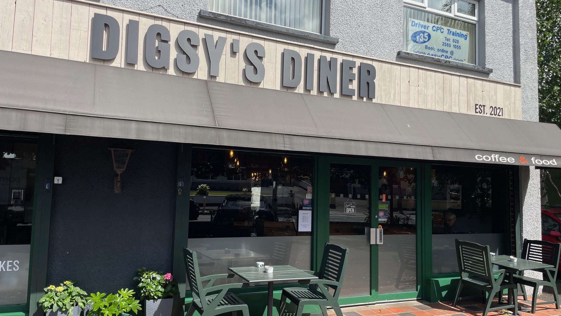 Grey, brown and green exterior of Digsy's Diner with green outdoor seating and plants