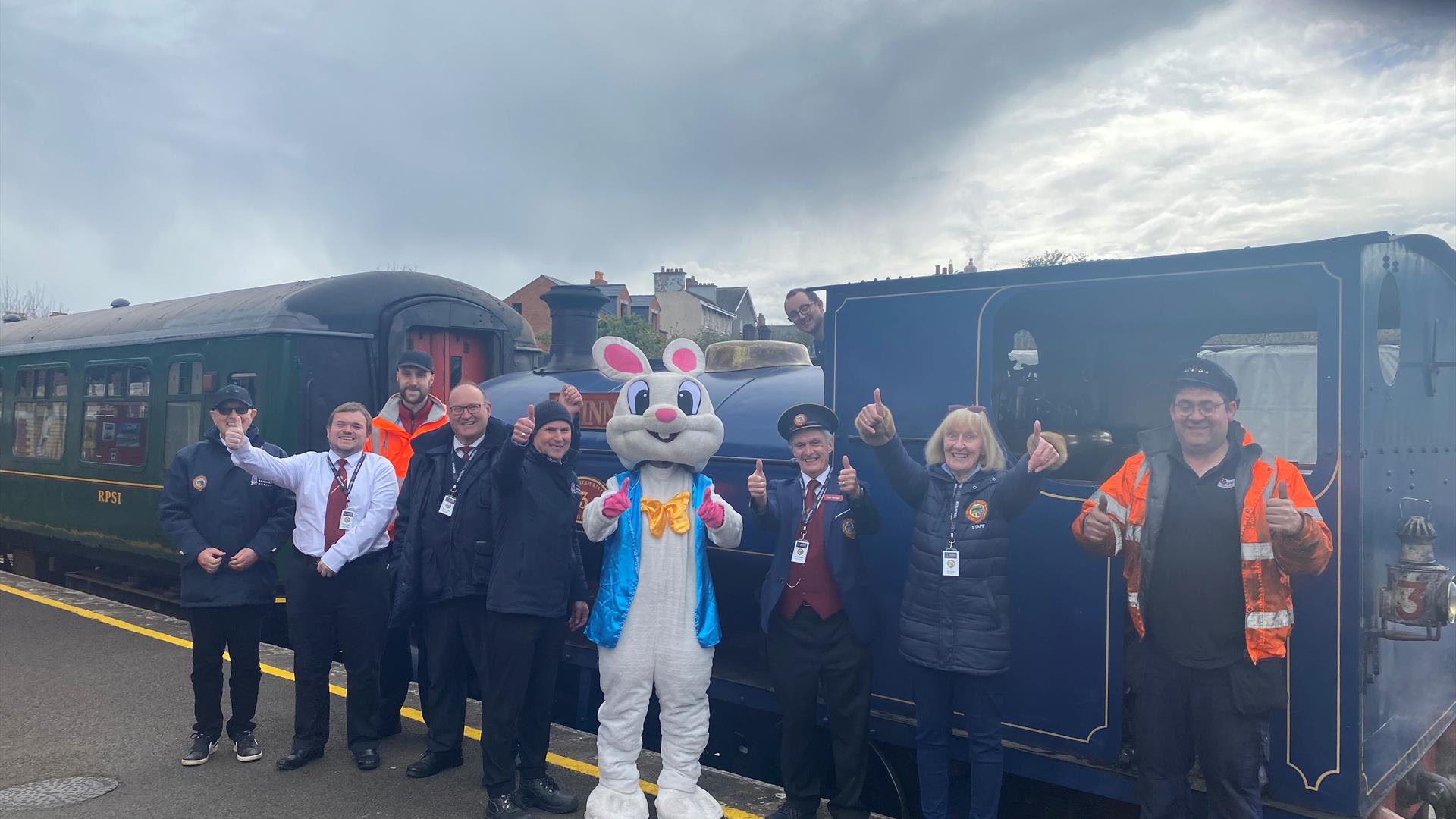 Group of volunteers with Easter Bunny standing outside steam train at Whitehead Railway Museum