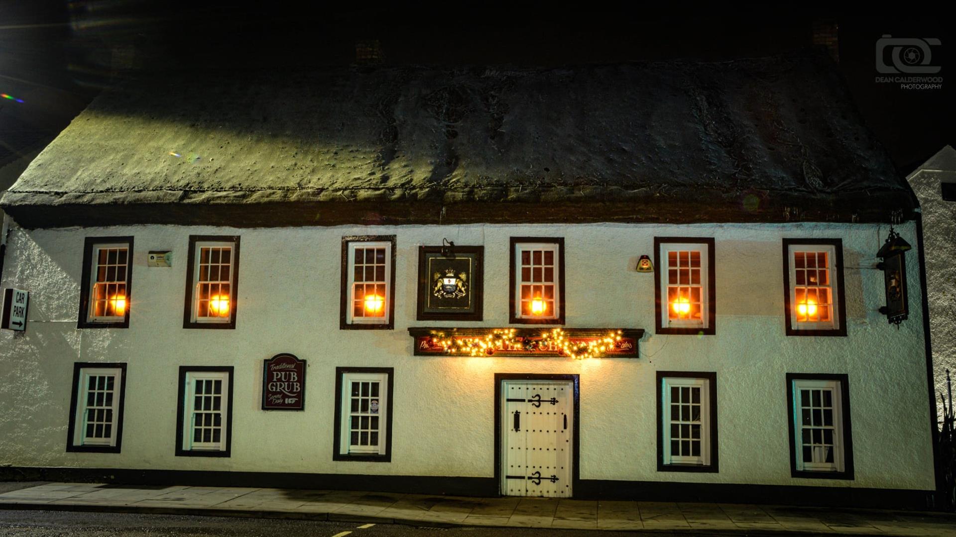 Night time exterior of the Thatch Inn Bar & Restaurant - white building with thatched roof and lights on in the upper windows