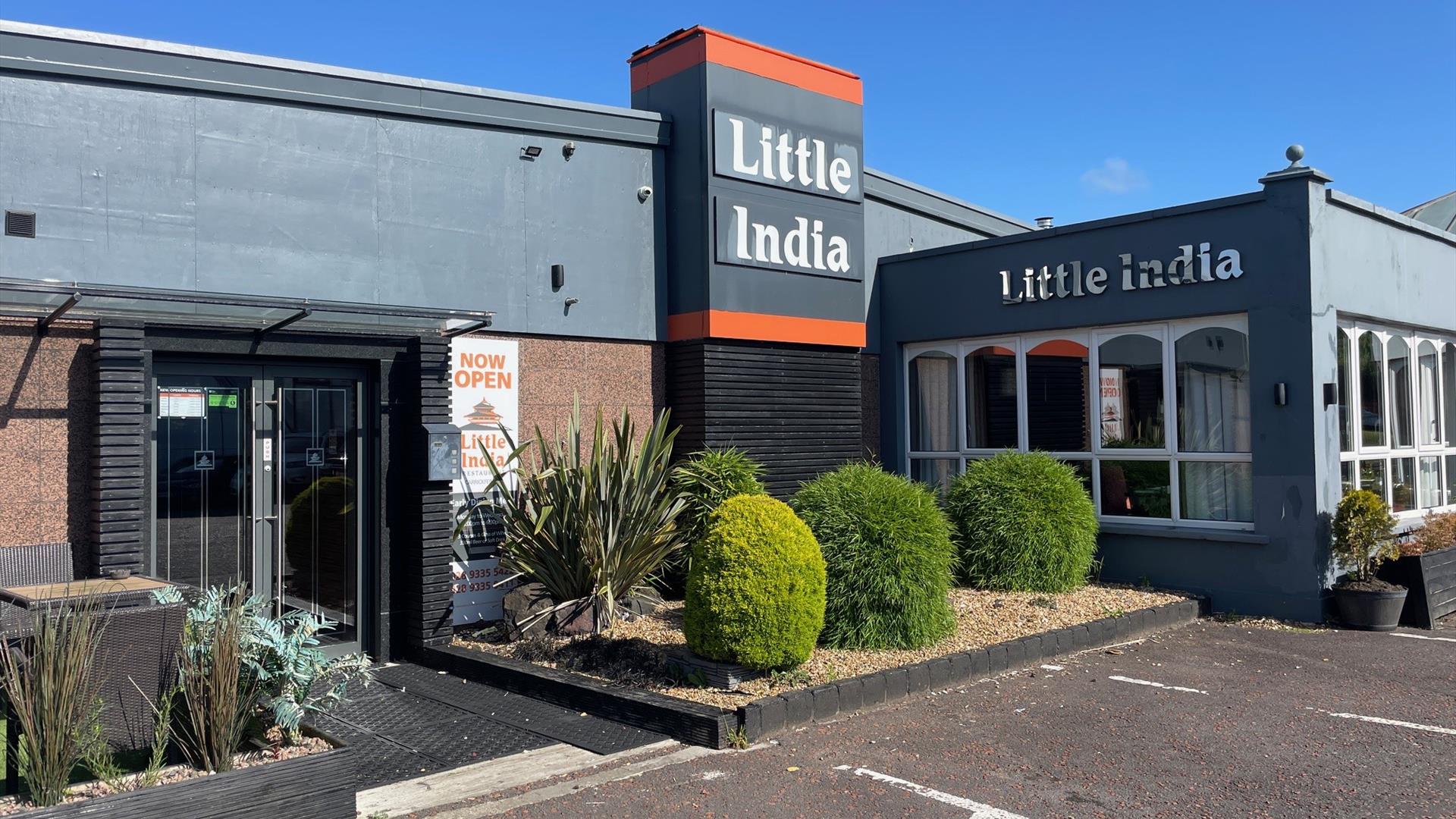 Exterior of Little India Restaurant with grey walls and name in silver, plus plants at the entrance doors