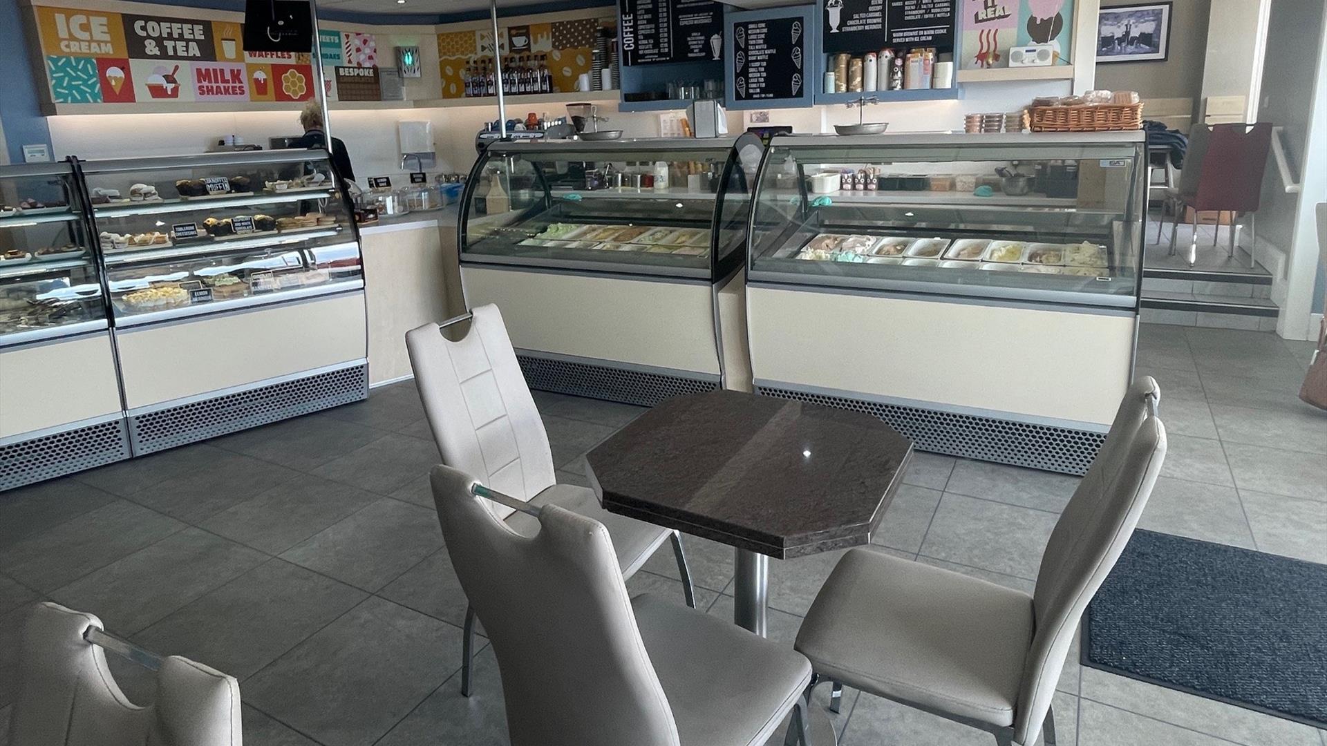 Grey seats and table with ice cream counters and food display fridges in the background