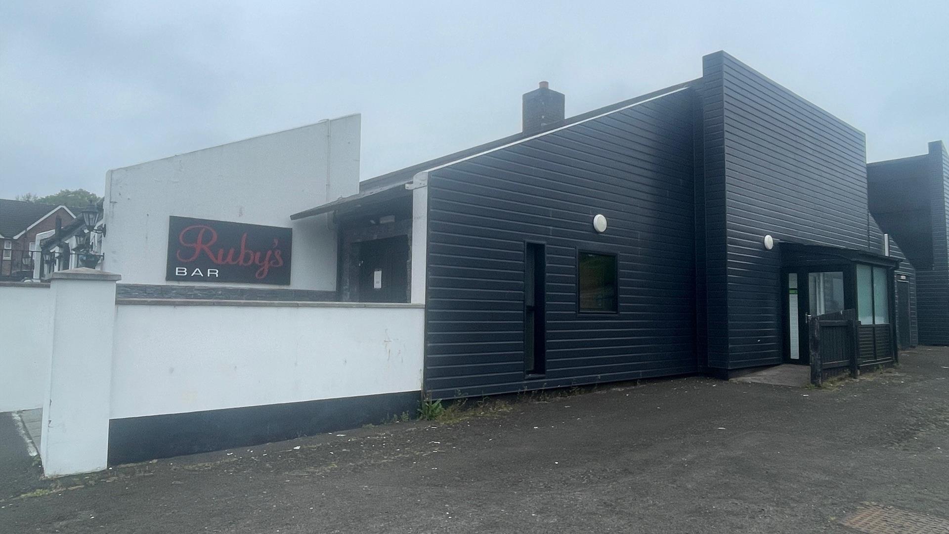 Black and white exterior of Ruby's Bar in Larne with sign featuring red name