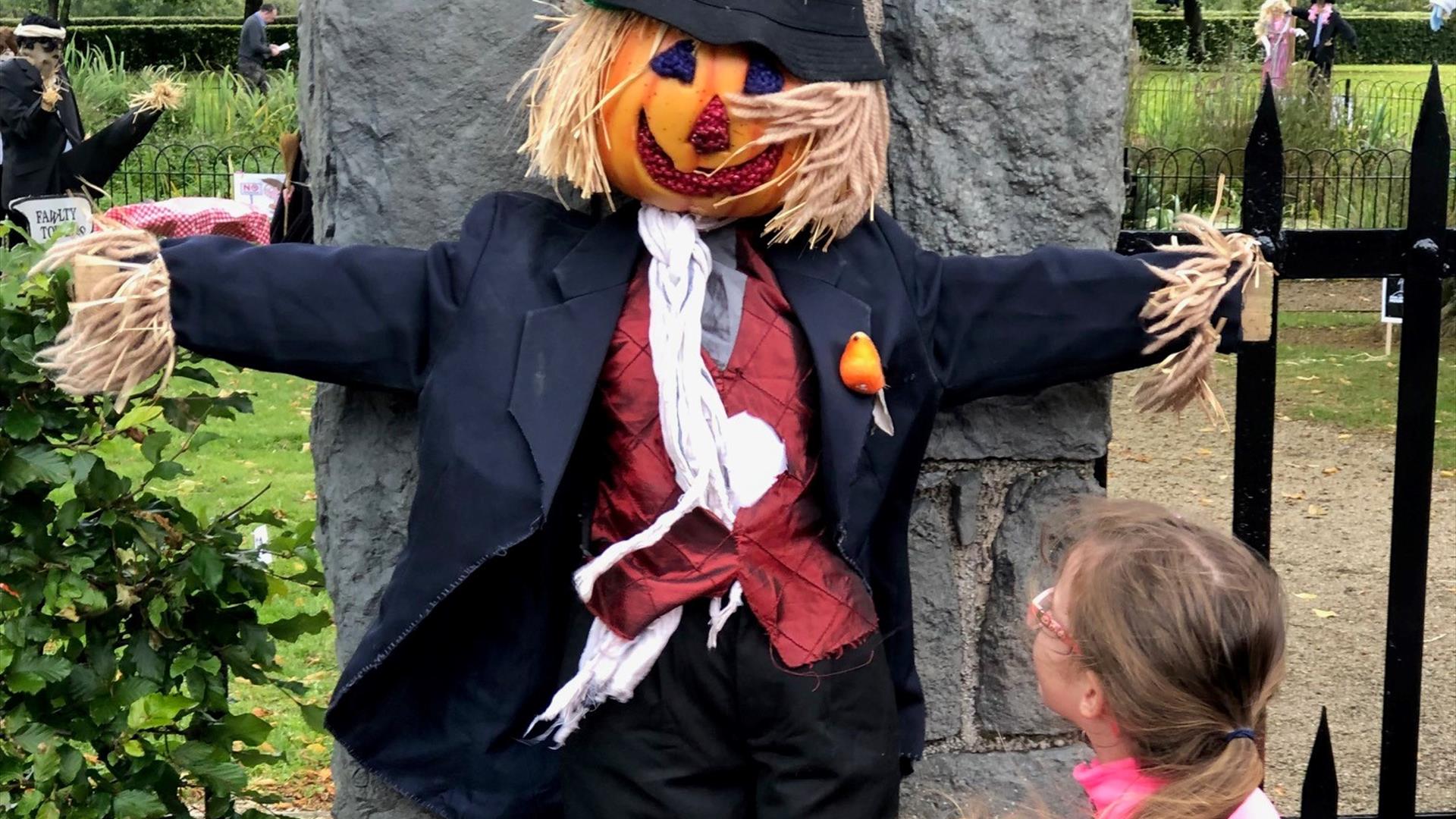 Little girl looking at a traditional scarecrow hanging on a gate pillar at Gracehill Scarecrow competition