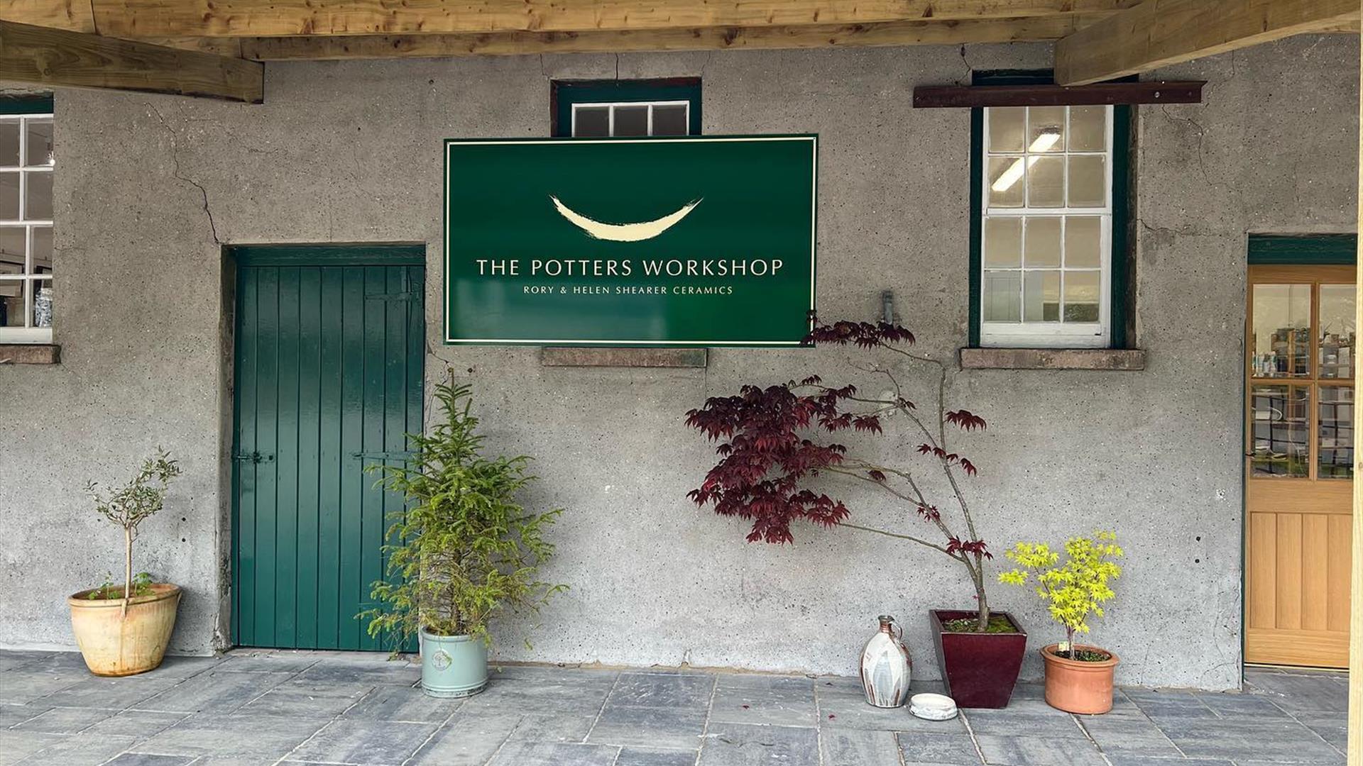 Entrance to Shearer Cermaics in grounds ofo Glenarm Castle with green door, grey paving, grey walls and green sign stating 'The Potters Workshop'