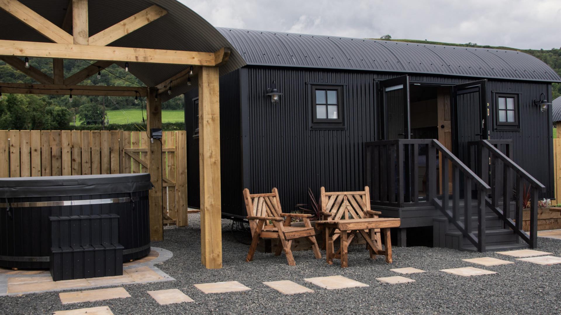 Hot tub beside a black Shepherds Hut with step entrance and seats outside at Shepherds Rest Luxury Glamping in Carnlough