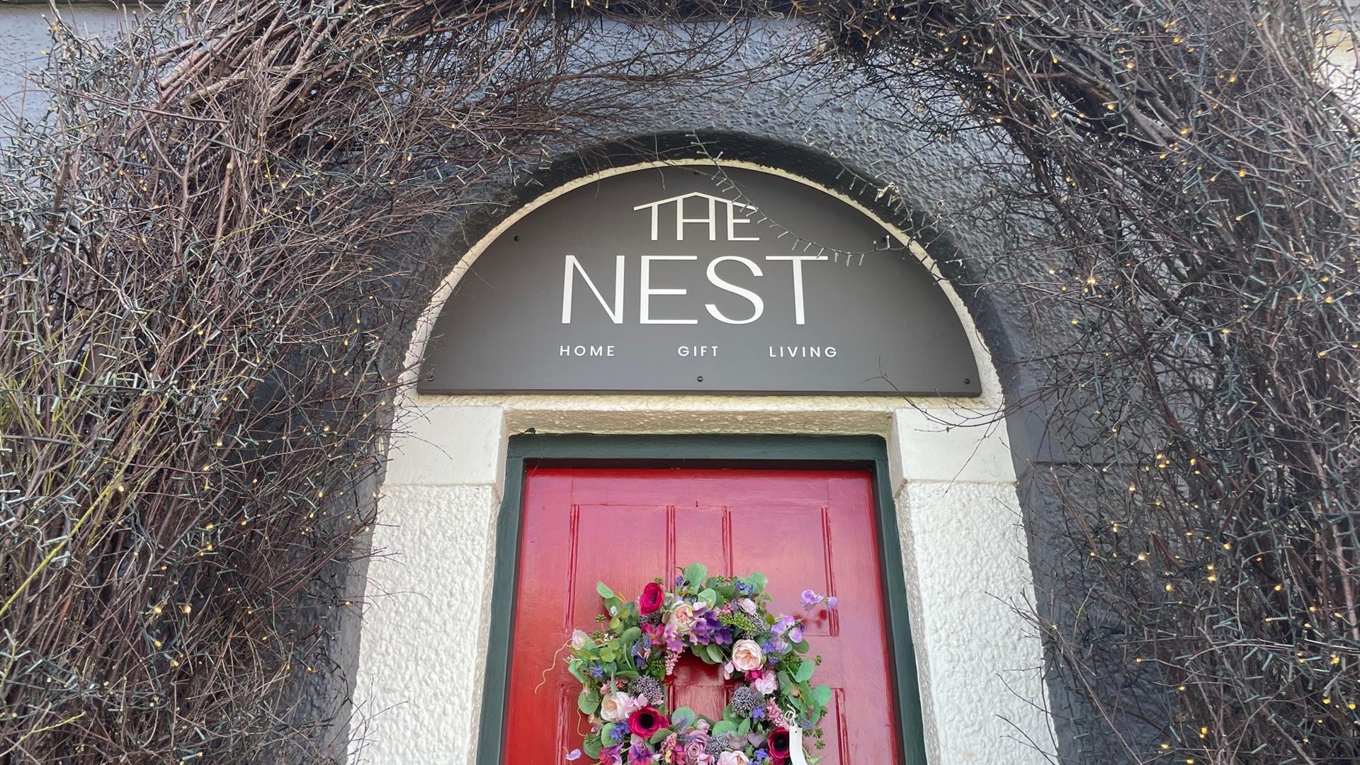 Archway over red door with sign reading The Nest and garland on the door