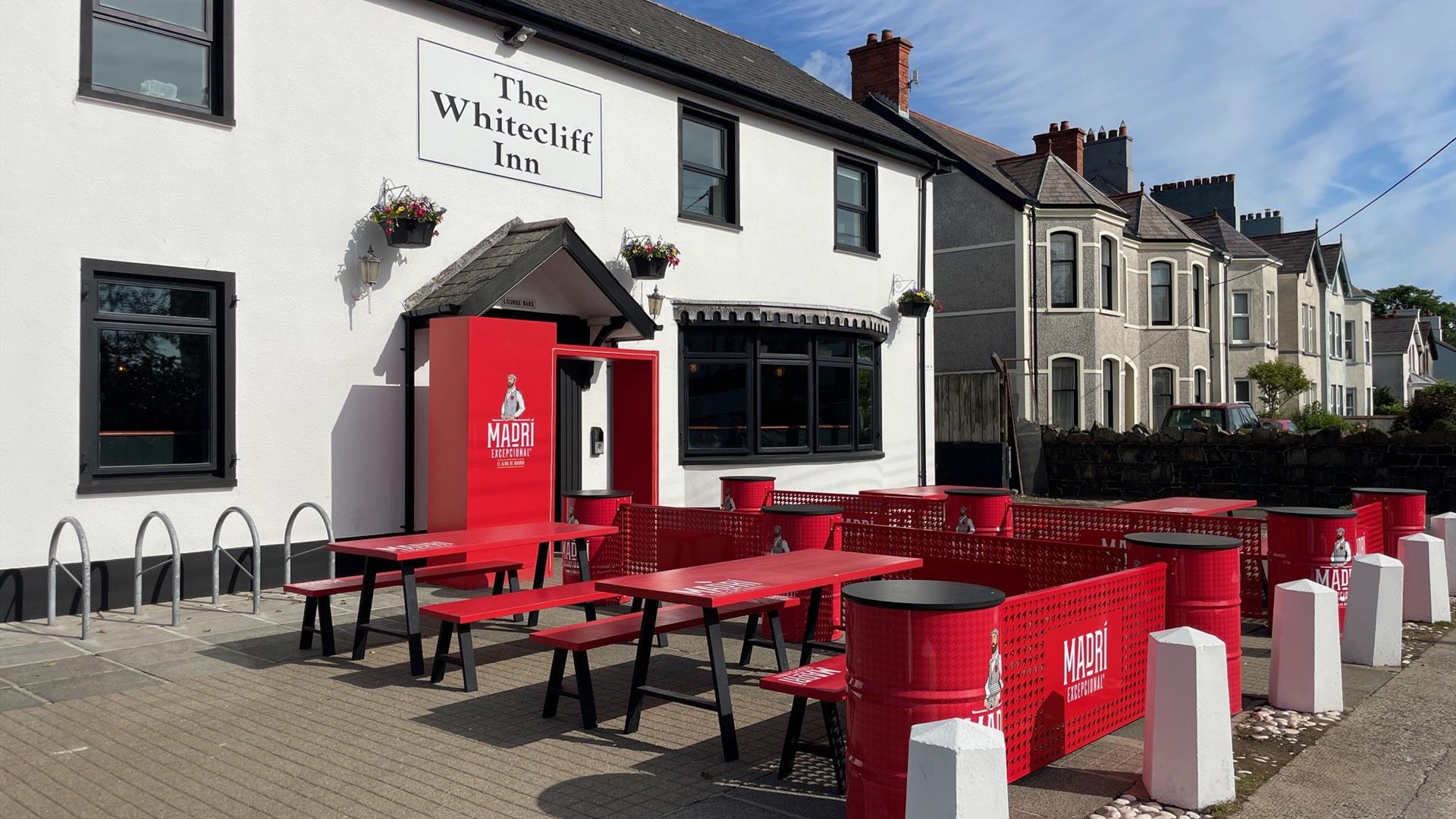 Exterior of Whitecliff Inn with red tables and chairs for seating area.
