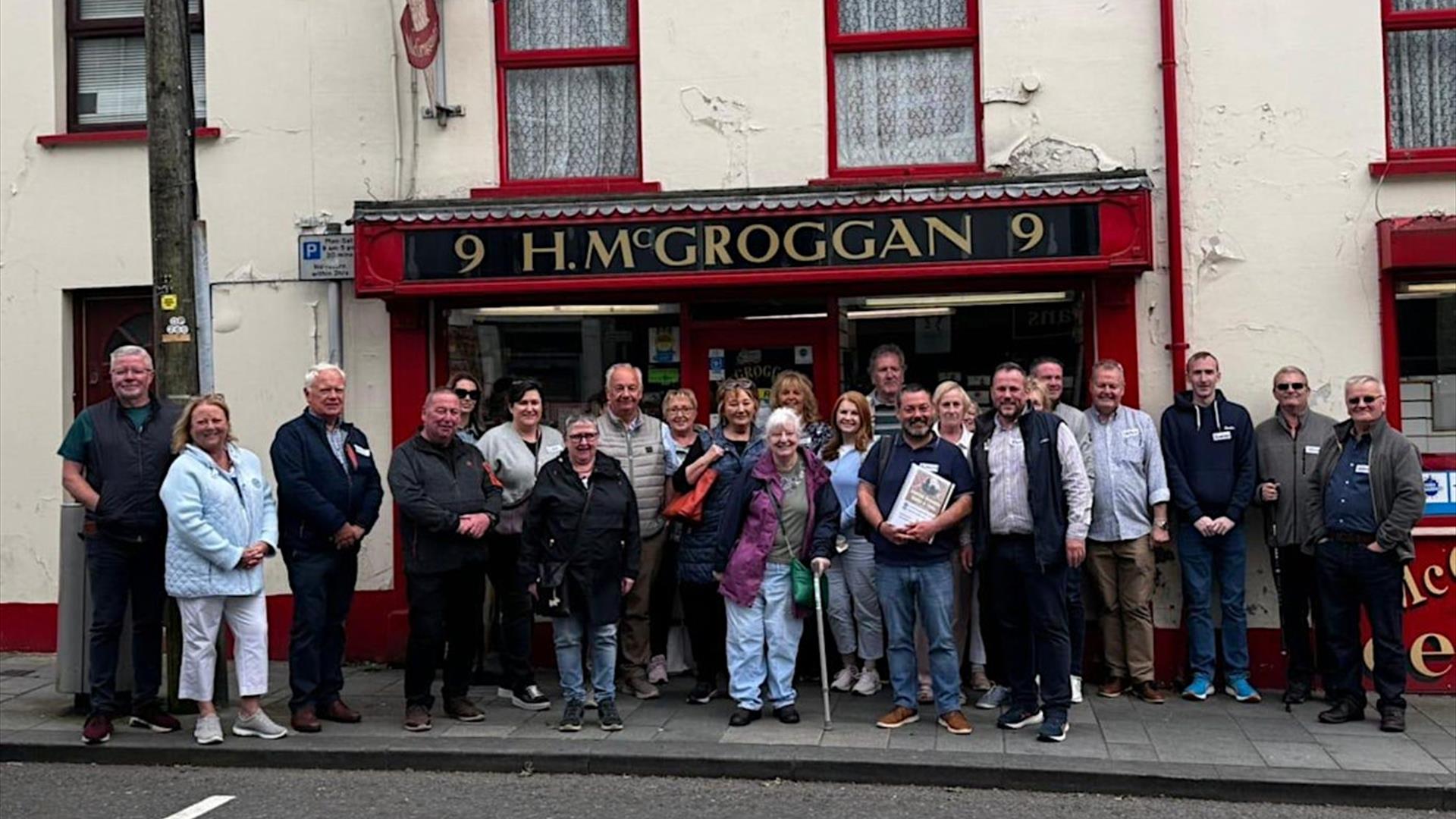 A group of people standing outside an old pub, on a walikng tour of Ballymena