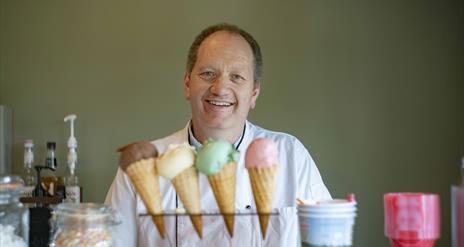 Man smiling standing in front of 4 different ice-creams.