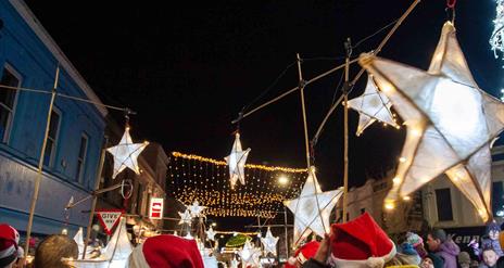 People parading with star lanterns and wearing Santa hats in Ballymena town centre with Christmas lights switched on.