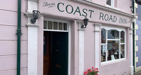 Pink exterior of Coast Road Inn in Glenarm with flowers outside and collectible window display
