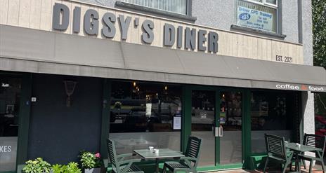 Grey, brown and green exterior of Digsy's Diner with green outdoor seating and plants