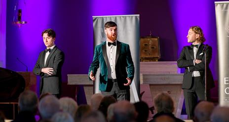 3 individuals in suits performing opera in a church venue