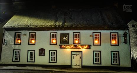 Night time exterior of the Thatch Inn Bar & Restaurant - white building with thatched roof and lights on in the upper windows