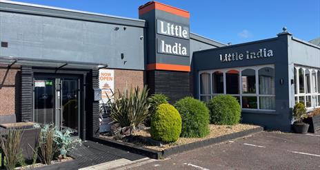 Exterior of Little India Restaurant with grey walls and name in silver, plus plants at the entrance doors