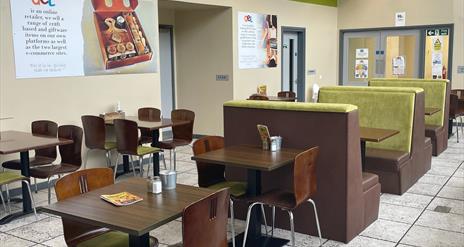 Wooden tables and seats, some with lime green backing within Lunchbox Cafe Larne