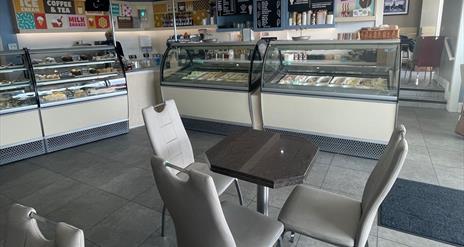 Grey seats and table with ice cream counters and food display fridges in the background
