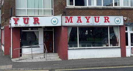 Exterior of Mayur Indian restaurant with sign in red and white, plus whote and red walls
