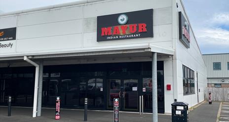 Exterior of Mayur Indian Restaurant in Larne with grey bulding and black windows / door