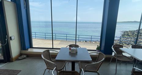 Table and seats within Prom Cafe looking out window to sea.