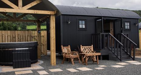 Hot tub beside a black Shepherds Hut with step entrance and seats outside at Shepherds Rest Luxury Glamping in Carnlough