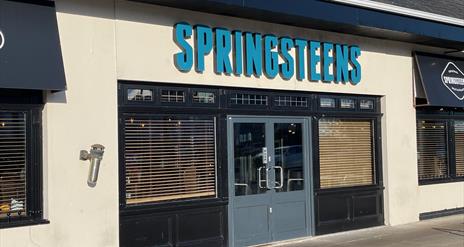 Exterior of Springsteens restaurant with grey doors and large sign.